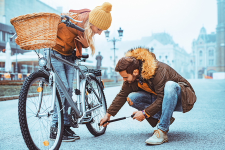 Close up of loving couple riding on bike in the city.Young man is filling his bike with air.の写真素材