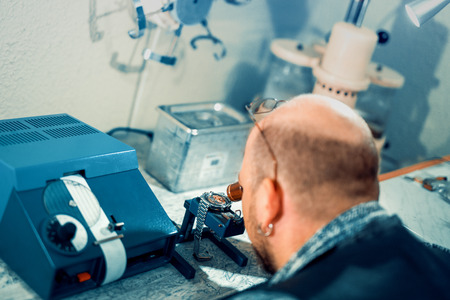 Close up portrait of a watchmaker at work.A watchmaker or repair man in action,viewing very closely a swiss watch.の写真素材