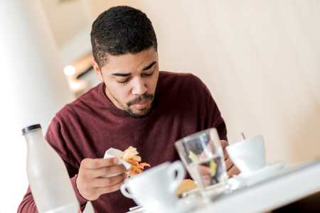 Handsome african american young man having breakfast in cafe.の写真素材