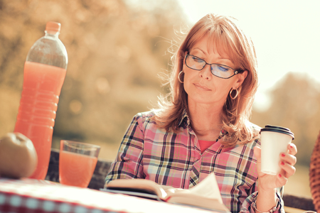 Happy mature woman reading a book during springtime in nature.の写真素材