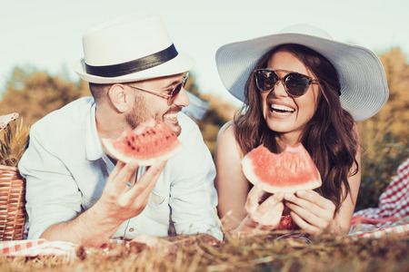 Happy couple on a picnic eating watermelon on a sunny day.の写真素材