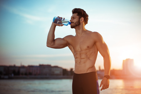 Portrait of young man drinking some water from a bottle and resting after training.の写真素材
