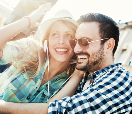 Happy couple with headphones sharing music from a smart phone on the street.の写真素材