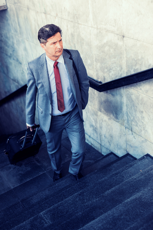 Elegant businessman walking with suitcase outside airport,business travel.の写真素材