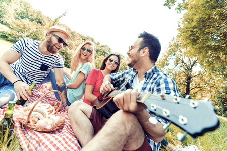 Happy young friends having picnic in the park.They are all happy,having fun,smiling and playing guitar.の写真素材