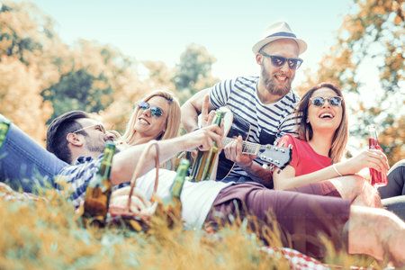 Happy young friends having picnic in the park.They are all happy,having fun,smiling and playing guitar.の写真素材