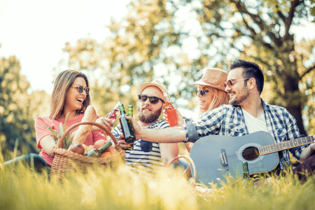 Happy young friends having picnic in the park.They are all happy,having fun,smiling and playing guitar.の写真素材