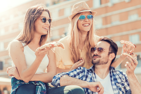 Close-up of four young cheerful people eating pizza.Group of friends taking their slices of pizza.の写真素材