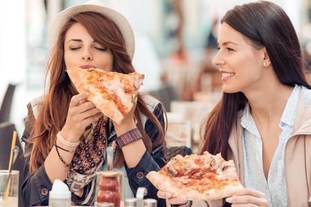 Two cheerful  girls eating pizza in a outdoor cafe.の写真素材