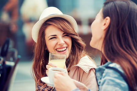 Two beautiful young girls sitting in a cafe, drinking lemonade and having a conversation.