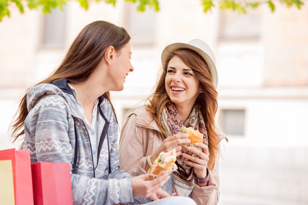 Two beautiful girls eating sandwich after shopping.の写真素材