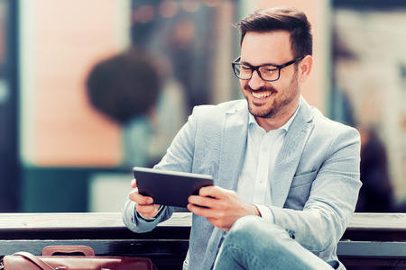 Close up portrait of a successful businessman using a digital tablet while sitting by a modern office building.の写真素材