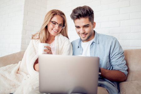 Couple watching a movie on laptop in their living room.Love, technology, internet and people concept.の写真素材