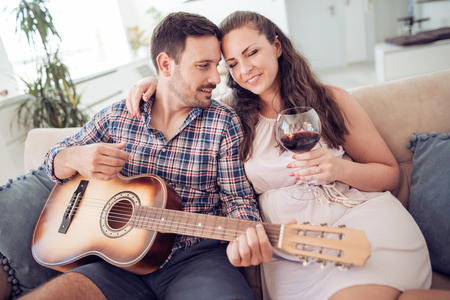 Man playing guitar in living room and woman listening,romantic moments.の写真素材