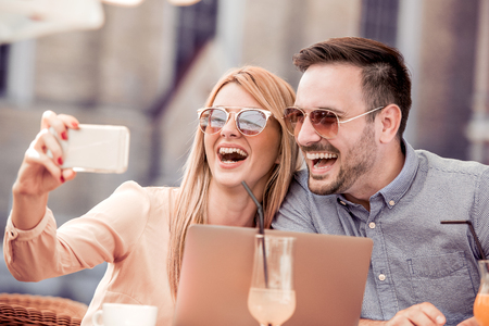 Lovely smiling couple taking selfie with smart phone while sitting in small cafe.の写真素材