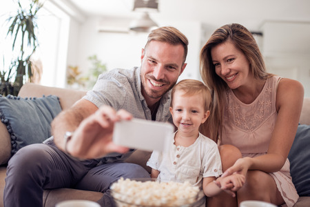 Happy couple with boy taking selfie while sitting on couch at home.の写真素材