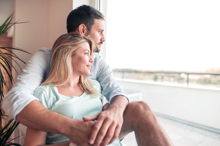 Beautiful young couple looks into the distance through the window.の写真素材