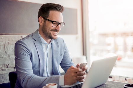 Portrait of young caucasian businessman in casual shirt and glasses using laptop computer at workplace.の写真素材