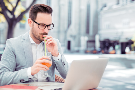 Young confident businessman in luxury suit having breakfast in modern coffee shop during work break,drink juice.の写真素材