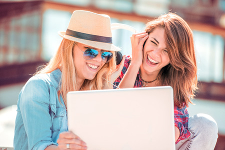 Two beautiful female music lovers in headphones enjoying popular musical compositions online with app on cellphone and laptop.の写真素材