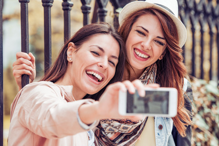 Portrait of two beautiful young women taking a selfie in the street.の写真素材