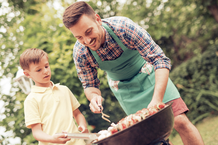 Happy father doing barbecue with his son on a sunny day.の写真素材