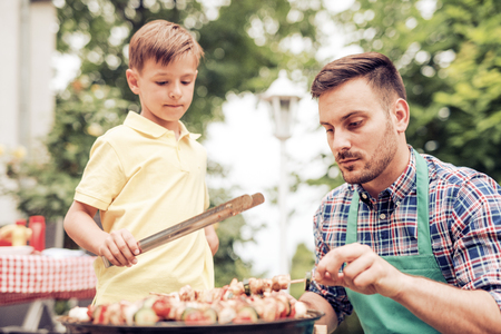 Happy father doing barbecue with his son on a sunny day.の写真素材