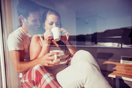 Portrait of happy couple drinking coffee by window at home.の写真素材