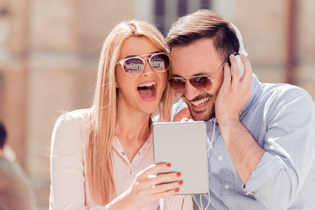 Happy young loving couple sitting outdoors together and looking at the tablet together.の写真素材