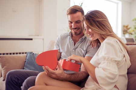 Happy young couple celebrating at home.Young man is giving his girlfriend a gift box.の写真素材