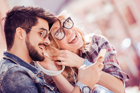 Young couple sharing and listening to music device,having fun outdoors.の写真素材