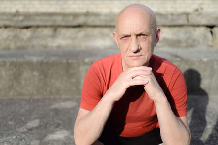 Retired man sitting on a concrete and look at the camera