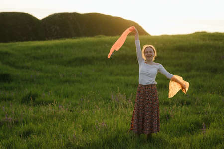 Beautiful red-haired girl is having fun and dancing in a field at sunsetの写真素材