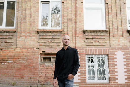 Young attractive man in a black shirt and standing next to brick house.の写真素材