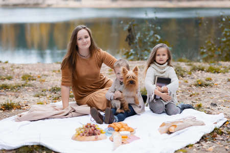 A young happy mother with two small children is having picnic in autumn park with colorful leaves.の写真素材