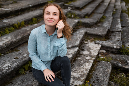 Ginger-haired girl sitting on old, weathered by elements stairs