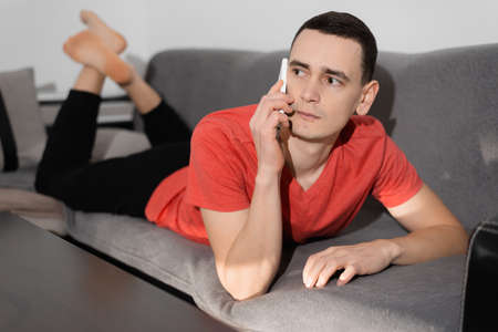A man using his cellphone while lying on the sofa at home