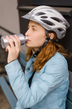 Girl cyclist, wearing a helmet, drinks water from a bottle.の写真素材