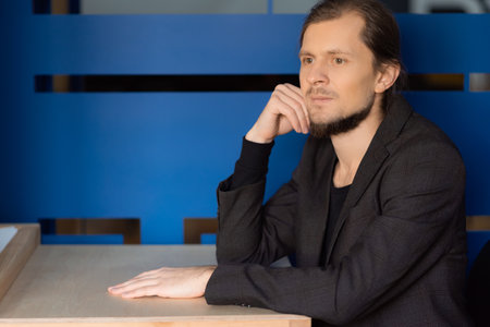 A man with long hair and a beard sits at a table and thinks about the work done