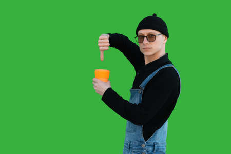 Happy young man in casual clothes on a background of green wall shows thumb up and holds eco cup and smiles while looking at the cameraの写真素材