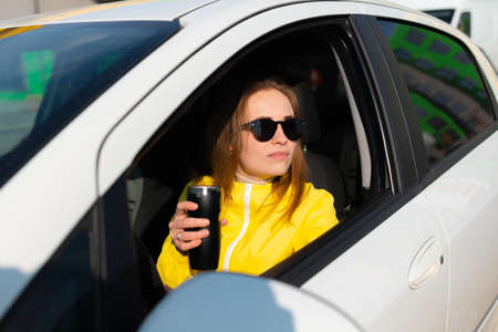 Portrait of smiling young woman is having coffee break in her car