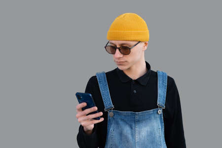 A young man uses smartphone on a gray background, looks into the screen with a smile on his face.の写真素材