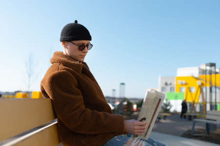 A man is reading the newspaper on a bench. The sky in the background.の写真素材