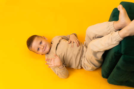 A boy is greeting lying on his back in a studio on a yellow backgroundの写真素材