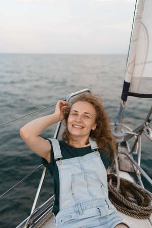 An attractive woman is looking at the camera and touching her red hair, lying on a yacht. Travel, tourism, and summer conceptの写真素材