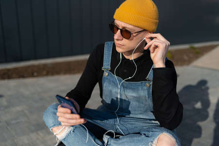 Young man relaxing on a bench in downtown district listening to music. high quality photoの写真素材