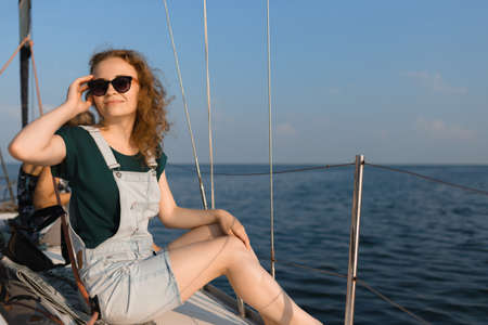 A young woman wearing stylish sunglasses is sitting on a yacht. The woman on summer vacation enjoying the view of the seaの写真素材