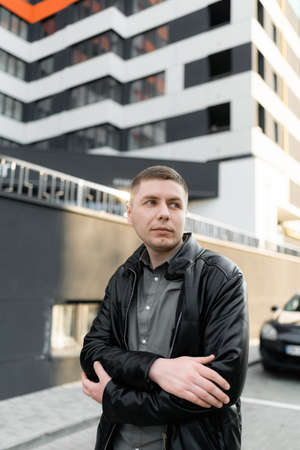 A man is standing in the parking lot with folded arms on his belt, looking to the side. street...