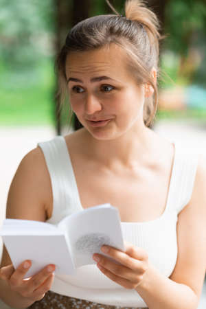 A young woman is reading a book and looking aside in surprise