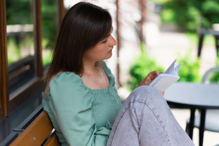 A woman enthusiastically reads her favorite book on the terrace of a street cafe.